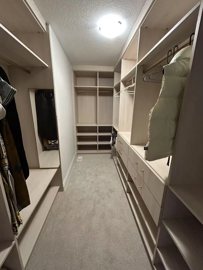 Custom walk-in closet with wood-tone shelving by Newood Millwork