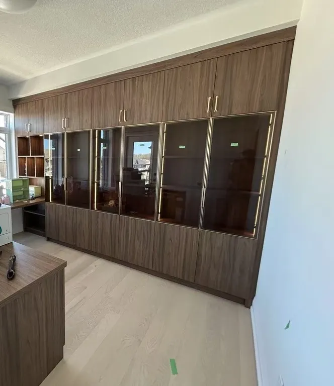 Custom home office with built-in desk and glass display cabinets by Newood Millwork
