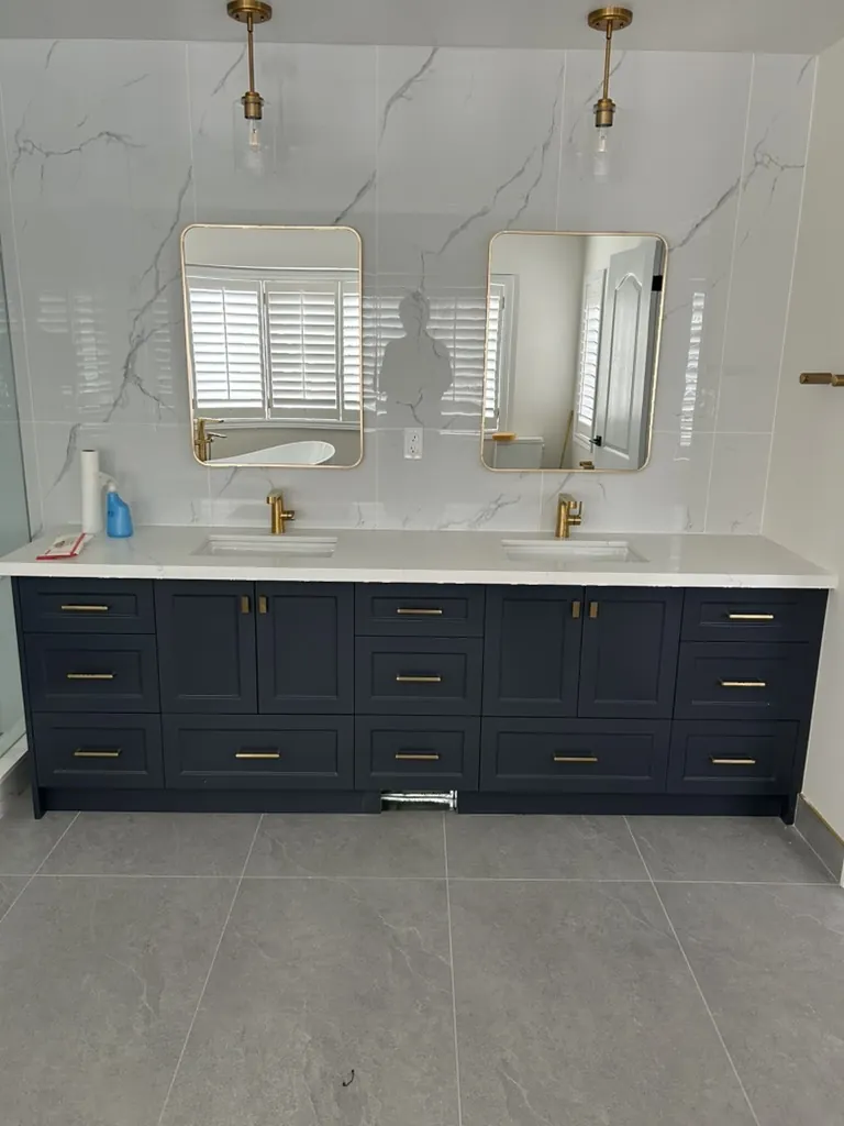 Custom navy double vanity with brass hardware and stone backsplash by Newood Millwork