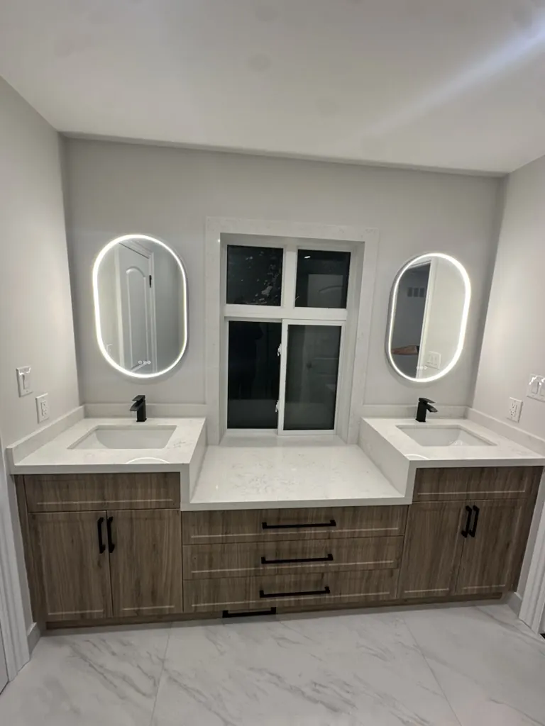 Custom wood-tone double vanity with LED mirrors by Newood Millwork